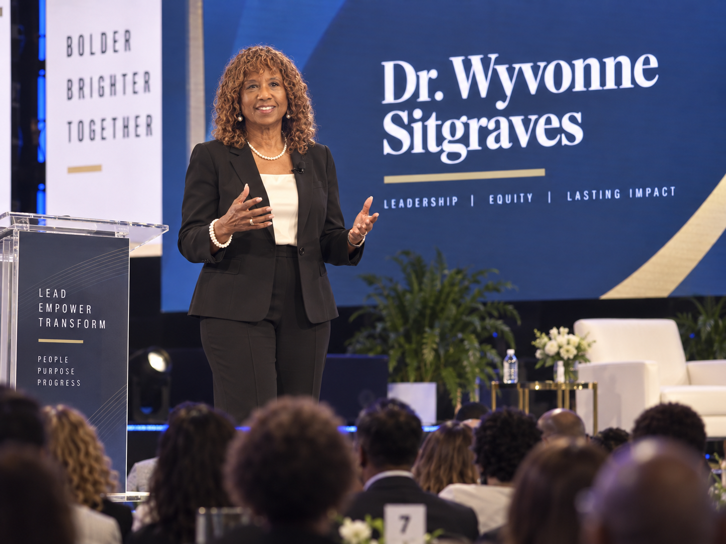 Dr. Wyvonne Sitgraves speaking at a podium in front of an audience, with a backdrop reading Leadership, Equity, Lasting Impact